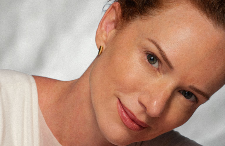 Foto de mujer inclinada semi recostada con la mano derecha tocando su hombro y luciendo un rostro terso